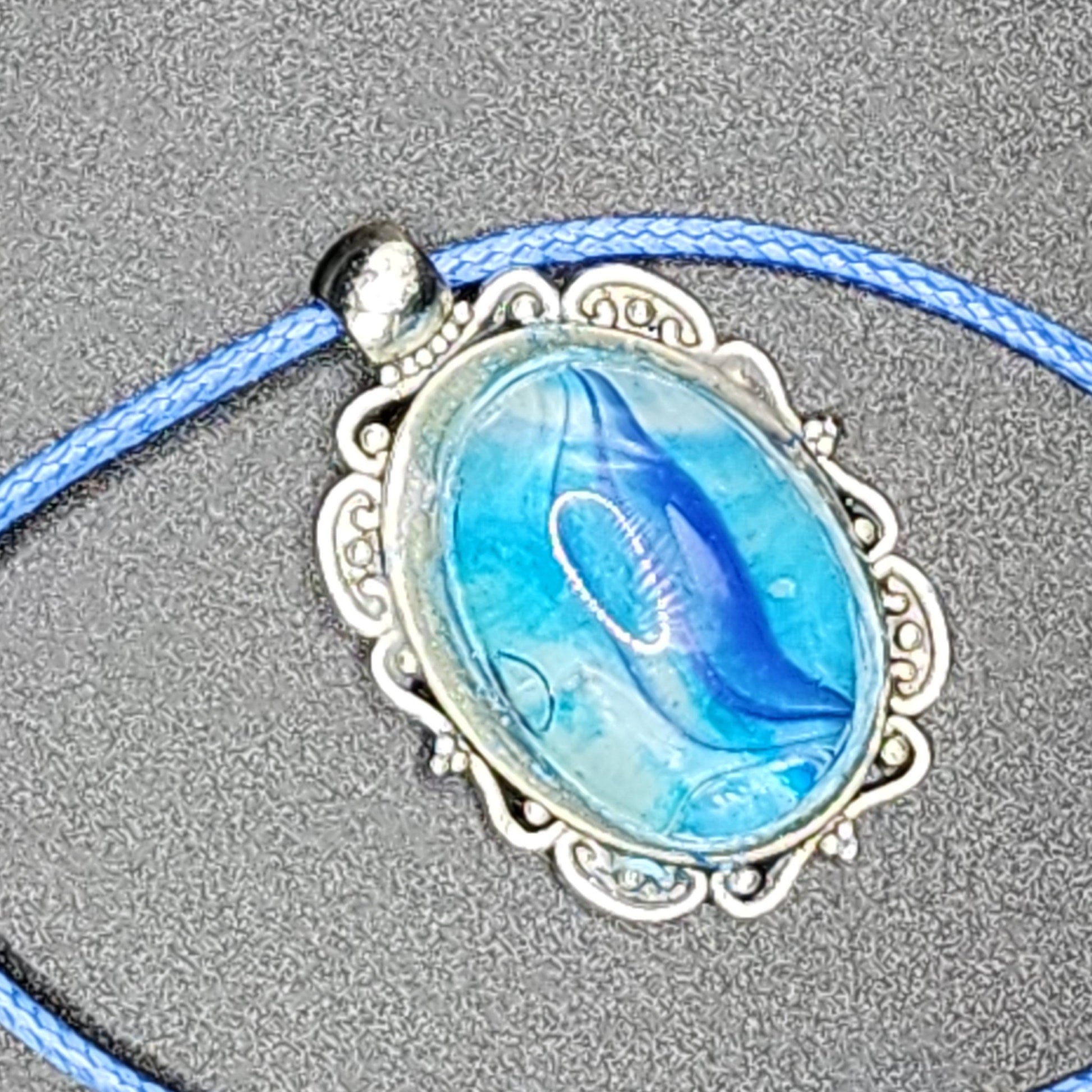 Ocean-inspired blue resin pendant necklace with antique-style silver frame and blue cord.