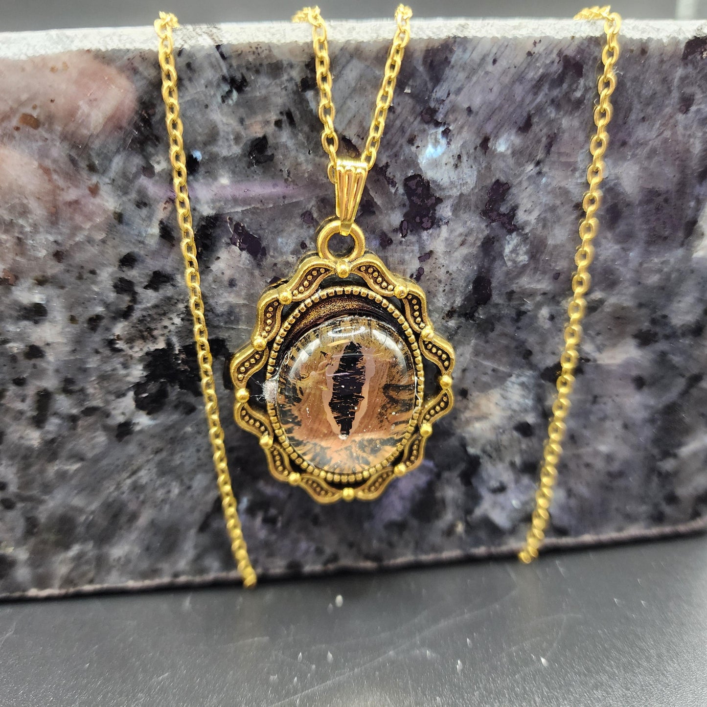 Gold-tone pendant necklace with a lifelike cat-eye design and ornate frame on a gold chain.