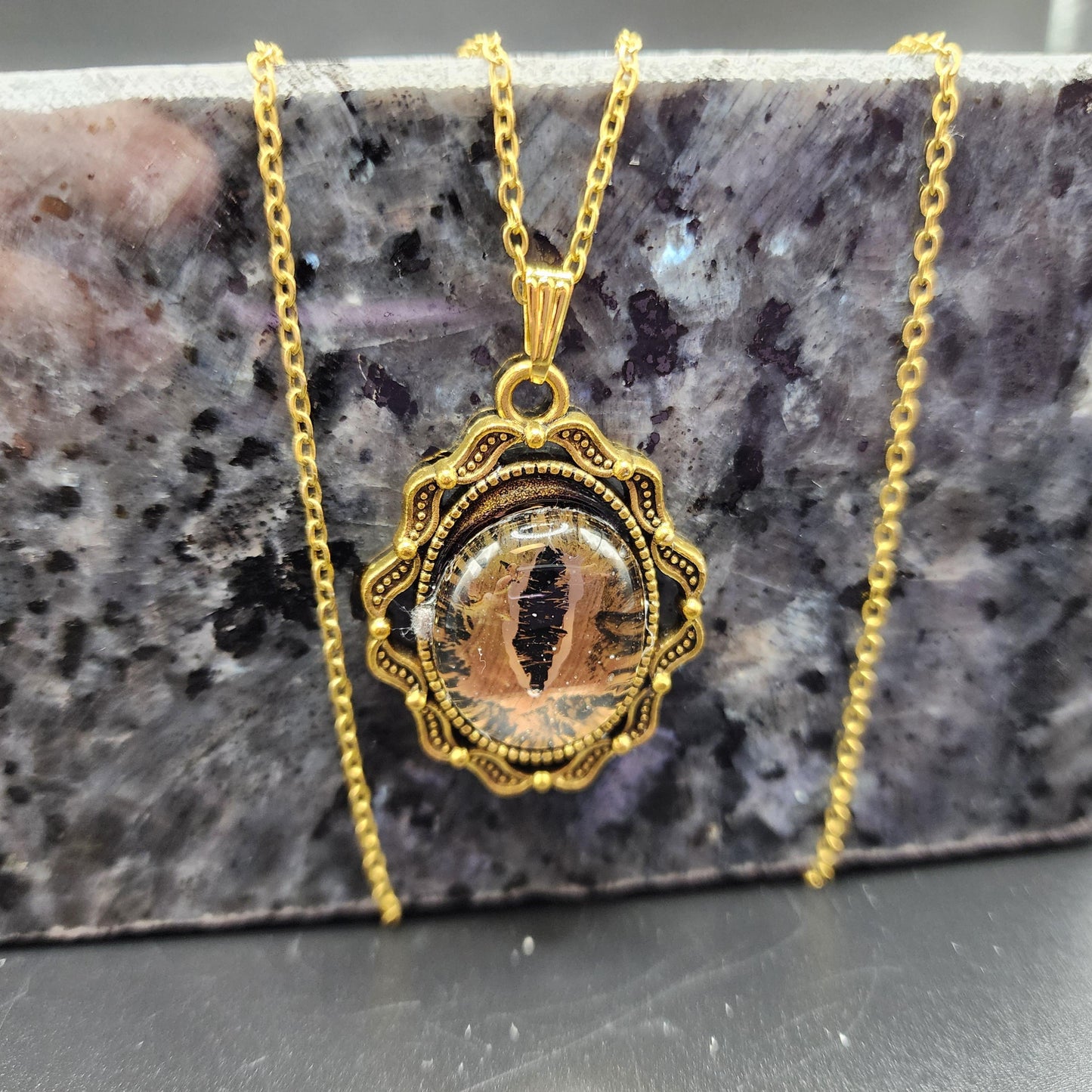 Gold-tone pendant necklace with a lifelike cat-eye design and ornate frame on a gold chain.