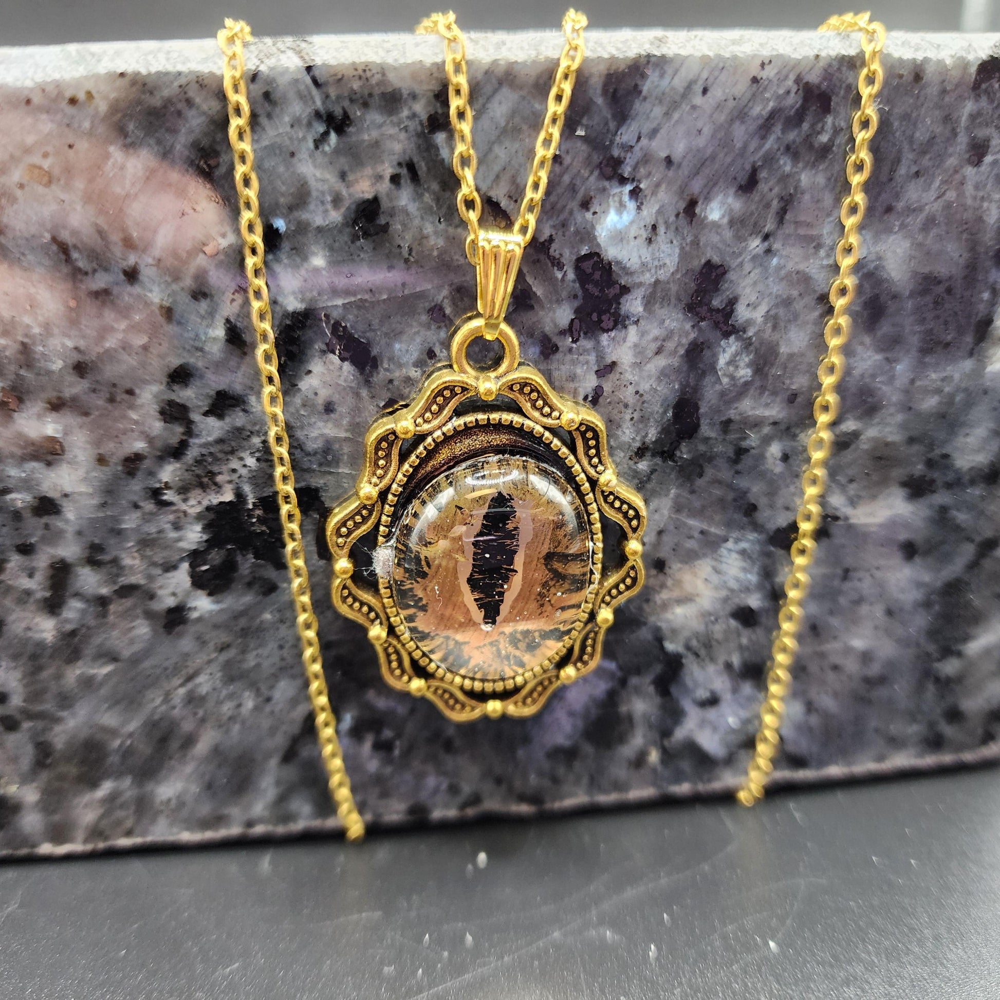 Gold-tone pendant necklace with a lifelike cat-eye design and ornate frame on a gold chain.