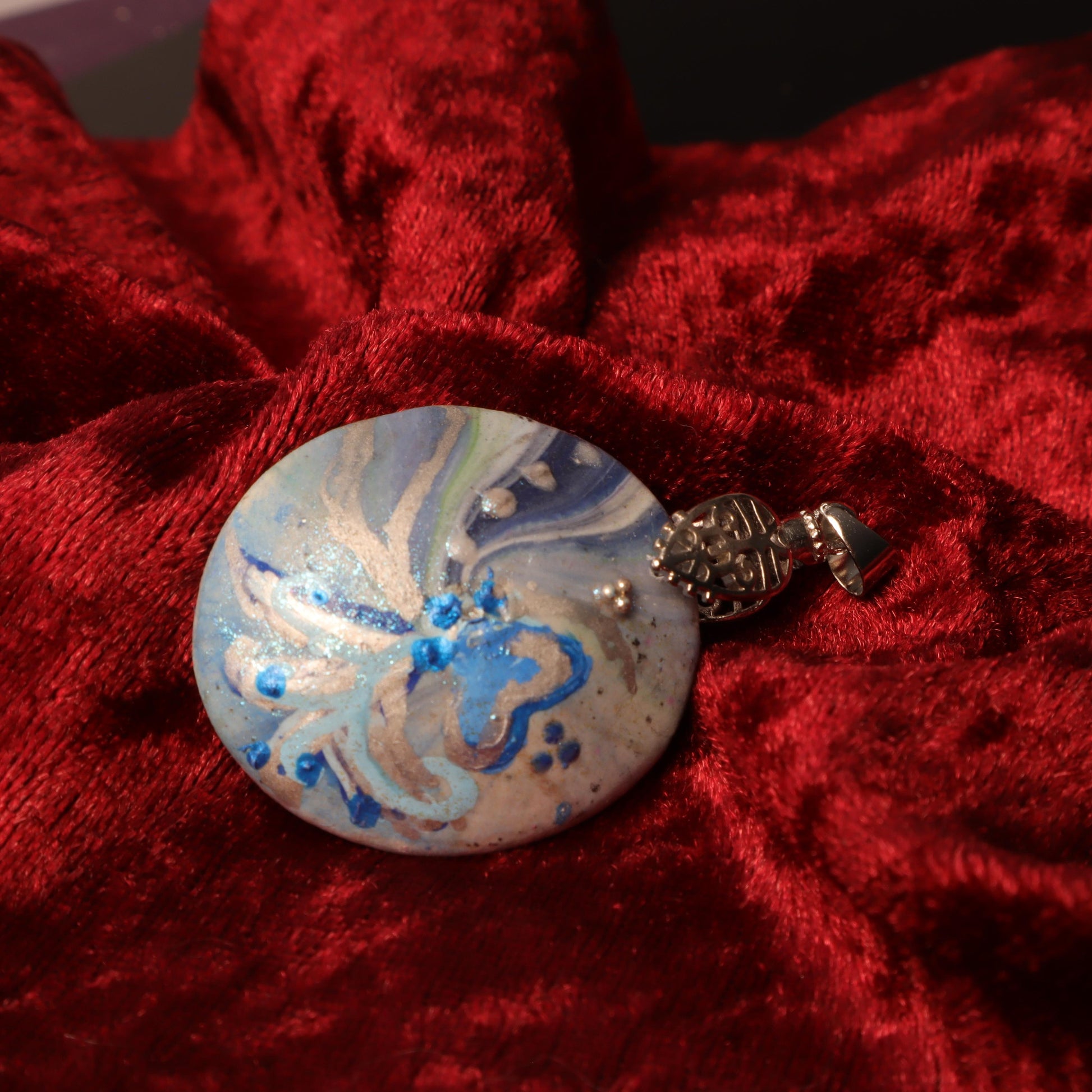 Close-up of a hand-painted polymer clay pendant with ocean-inspired swirls in blue and silver hues