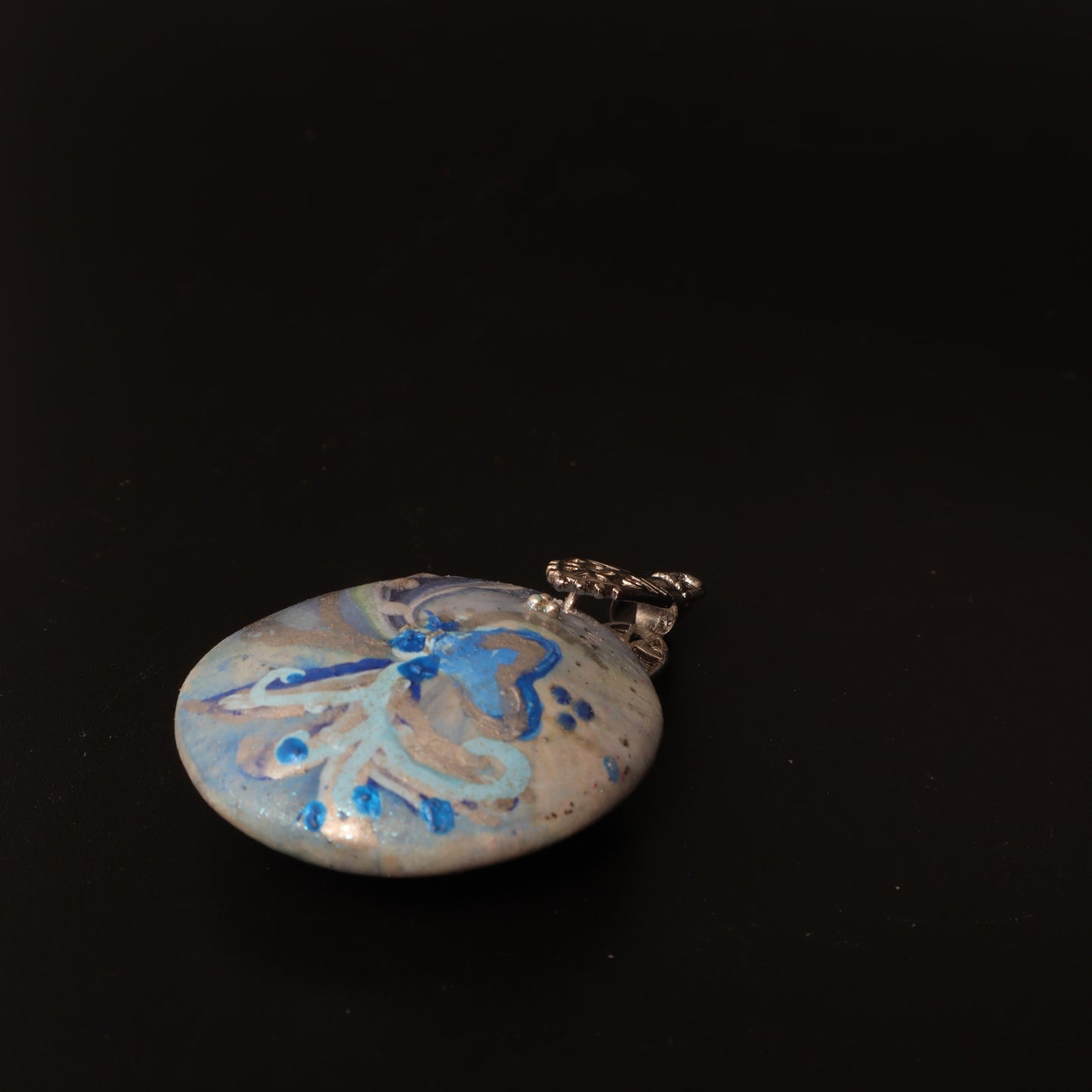 Close-up of a hand-painted polymer clay pendant with ocean-inspired swirls in blue and silver hues