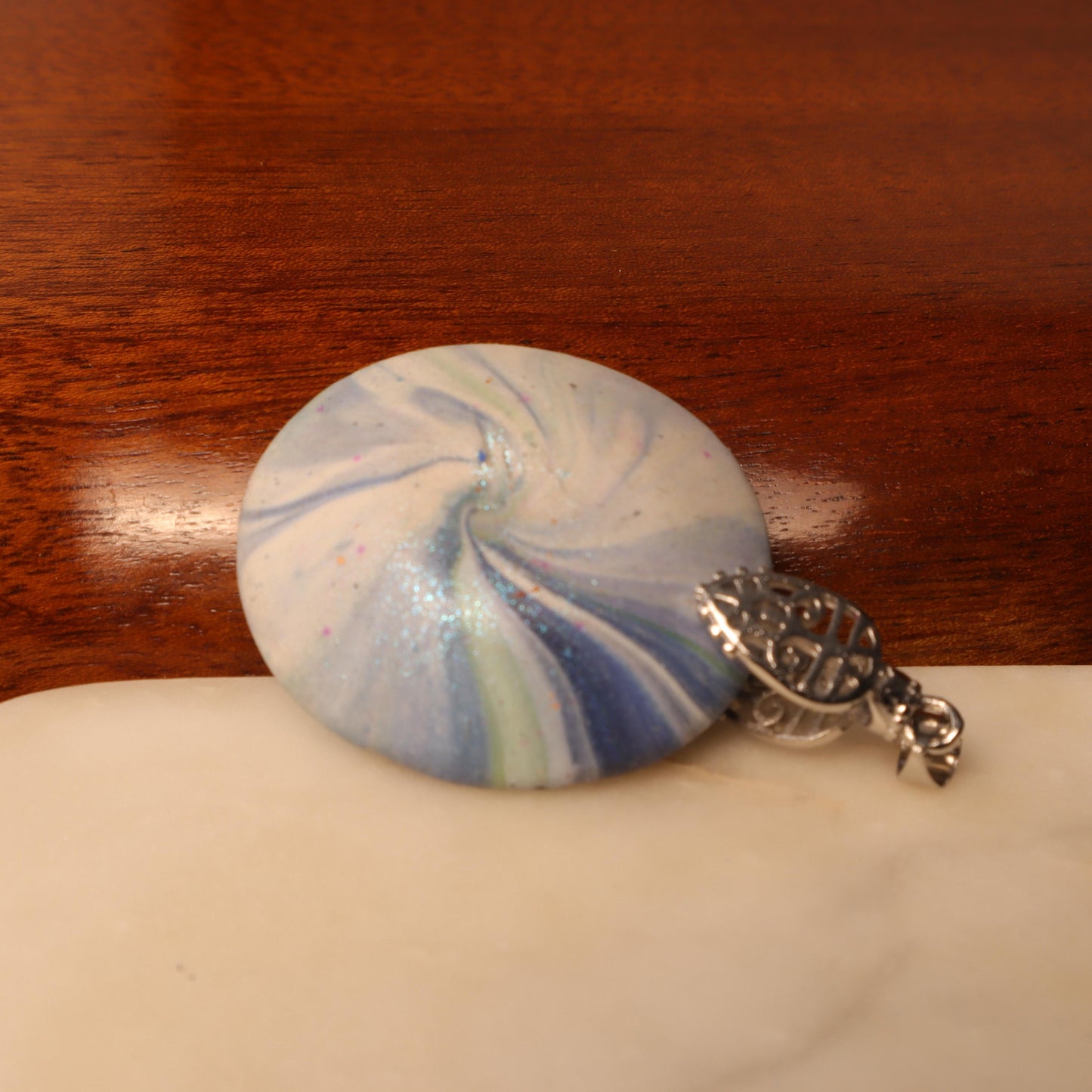 Close-up of a hand-painted polymer clay pendant with ocean-inspired swirls in blue and silver hues