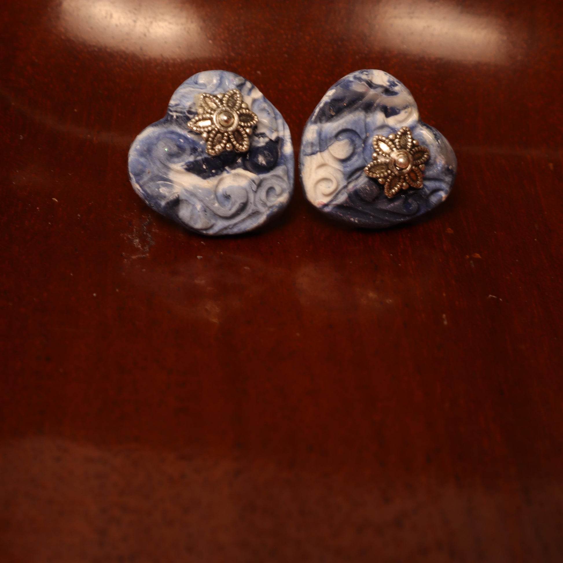 Heart-shaped polymer clay earrings in swirling blue and white patterns with silver flower accents