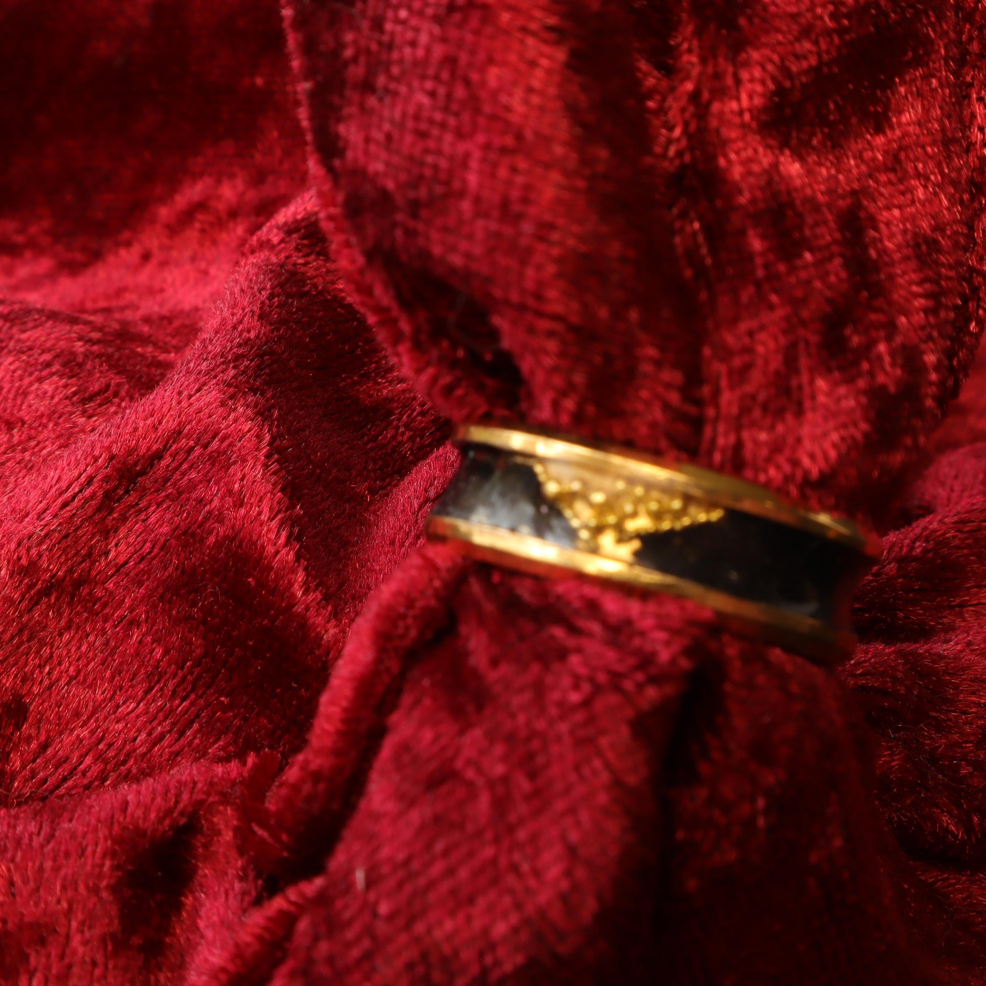 Handcrafted black resin ring with gold-tone bands displayed on a black stand, showcasing its sleek and luxurious design