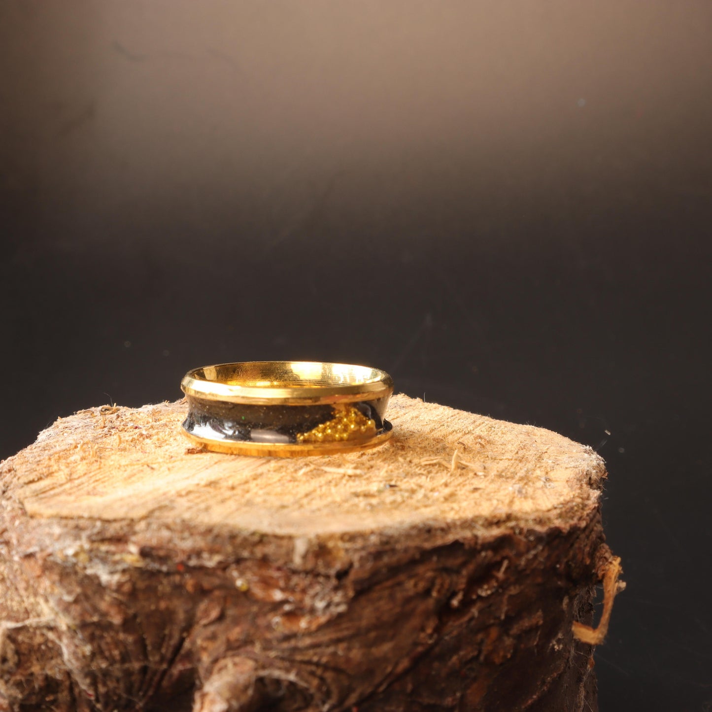 Handcrafted black resin ring with gold-tone bands displayed on a black stand, showcasing its sleek and luxurious design